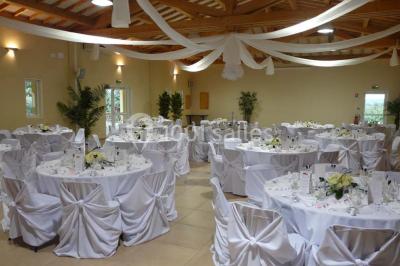Terrasse extérieure éclairée la nuit, avec des tables et chaises en fer forgé entourées de fleurs colorées.