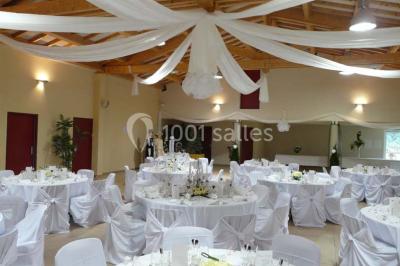 Terrasse extérieure éclairée la nuit, avec des tables et chaises en fer forgé entourées de fleurs colorées.