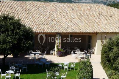 Terrasse extérieure éclairée la nuit, avec des tables et chaises en fer forgé entourées de fleurs colorées.
