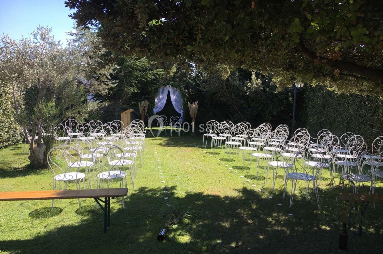 Chaises blanches disposées en allées sur une pelouse, entourées de végétation, avec une arche décorée en arrière-plan.