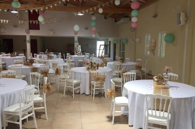 Terrasse extérieure éclairée la nuit, avec des tables et chaises en fer forgé entourées de fleurs colorées.