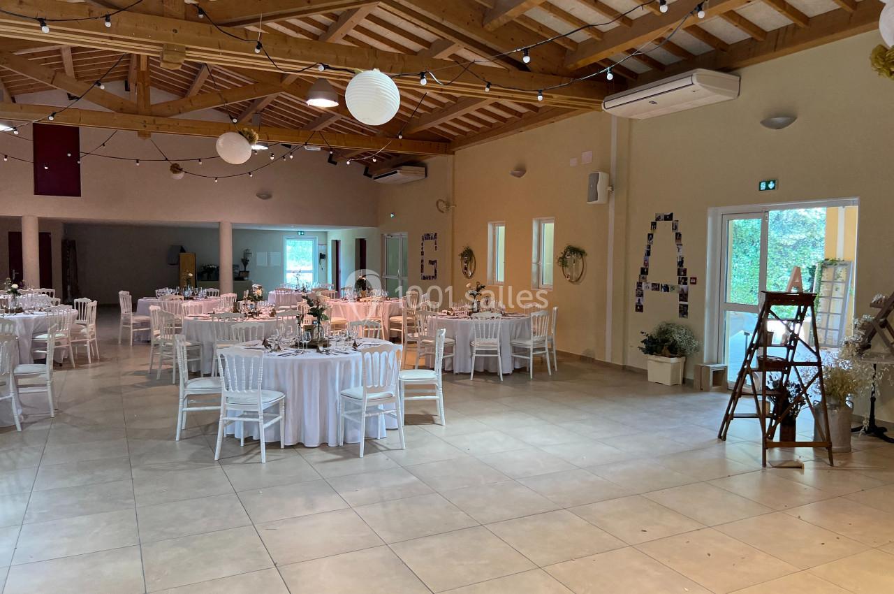 Salle de réception décorée avec des tables rondes dressées, des guirlandes lumineuses et des éléments décoratifs suspendus.