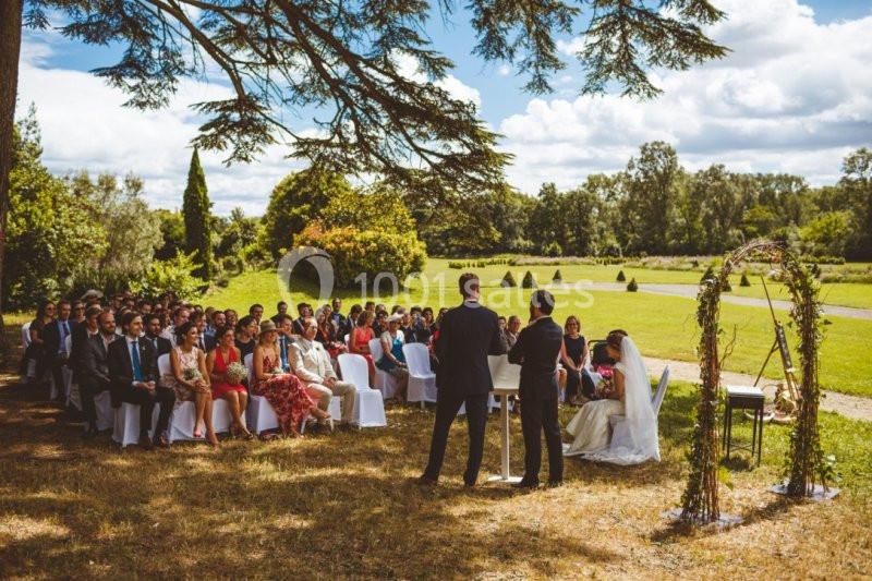 Cérémonie de mariage en plein air avec des invités assis, un officiant et un couple sous une arche décorée.