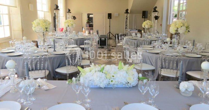 Salle de réception élégamment décorée avec des tables dressées, des fleurs blanches et des chaises transparentes.