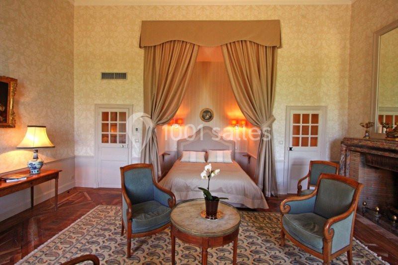 Chambre élégante avec lit à baldaquin, fauteuils anciens, cheminée et décoration classique dans des tons chaleureux.