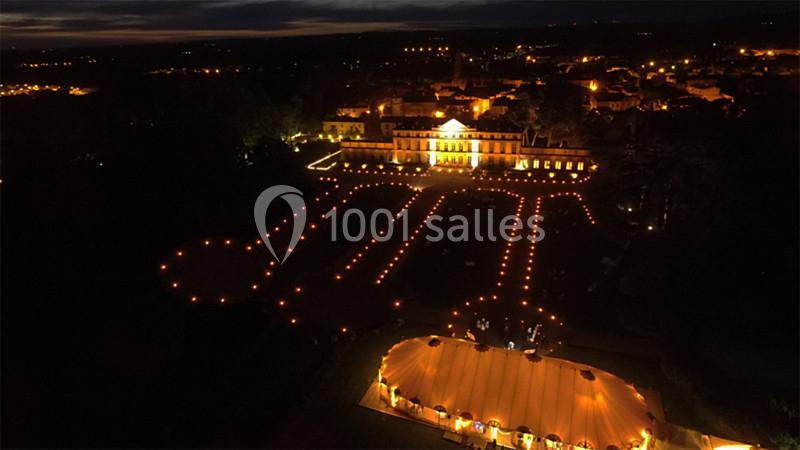 Vue aérienne nocturne d'un domaine illuminé avec une grande tente éclairée et des allées bordées de lumières.