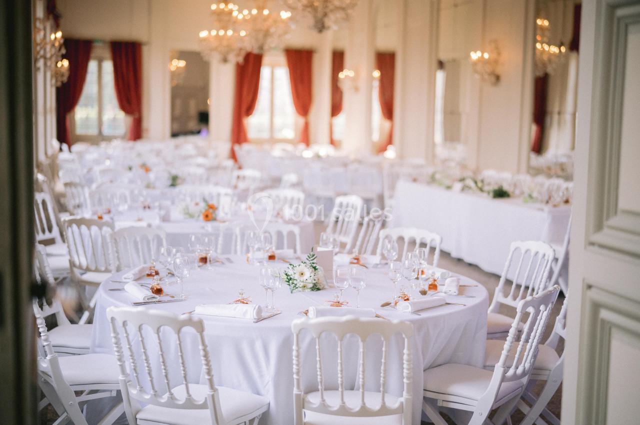 Salle de réception élégante avec tables rondes dressées, nappes blanches, chaises assorties et décorations florales.