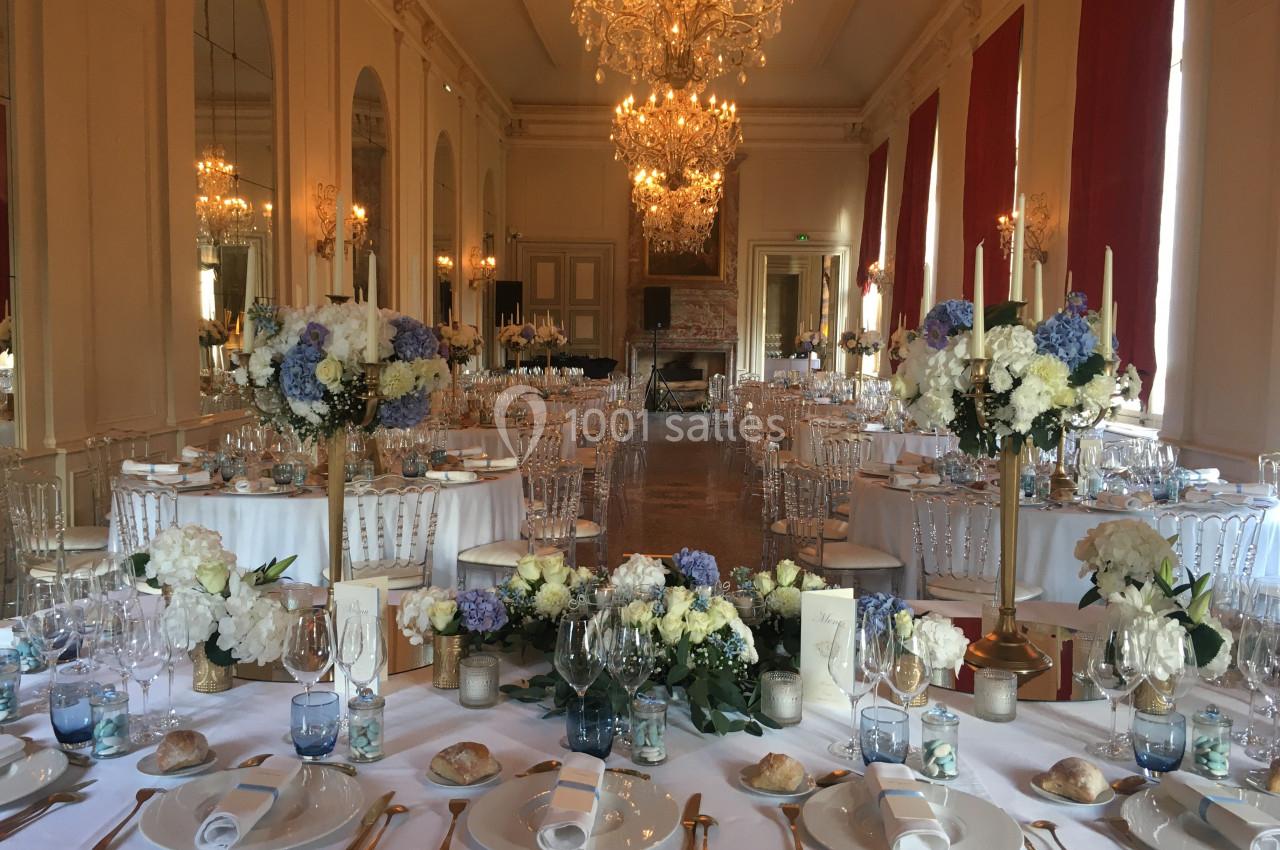 Grande salle élégante décorée pour un banquet, avec tables dressées, chandeliers et compositions florales.