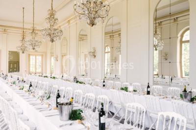 Salle de conférence élégante avec rangées de chaises blanches, lustres suspendus et écran de projection à l'arrière.