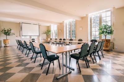 Salle de conférence élégante avec rangées de chaises blanches, lustres suspendus et écran de projection à l'arrière.