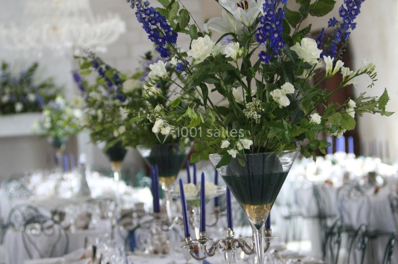 Grande table de réception élégamment dressée avec chandeliers, verres, et compositions florales bleues et blanches.
