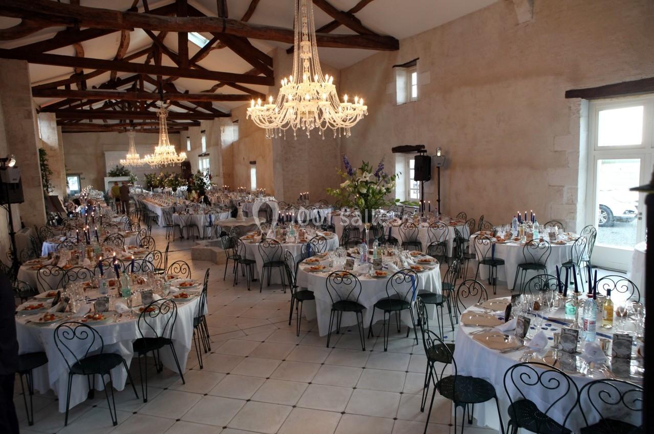 Salle de réception lumineuse avec tables rondes dressées, chaises en fer forgé et lustres suspendus.