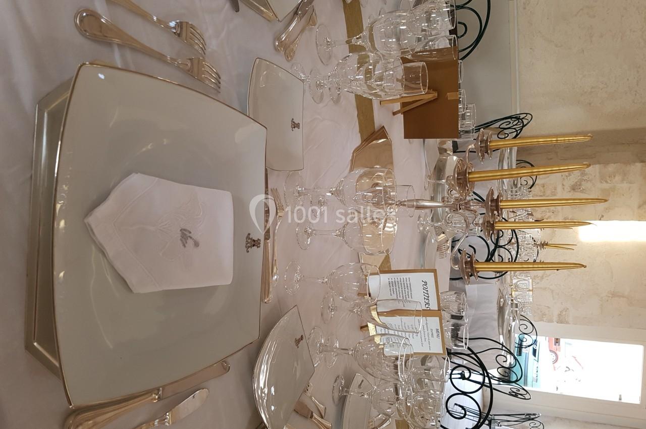 Table élégamment dressée avec assiettes carrées, serviettes pliées, verres à pied et bougeoirs dorés.