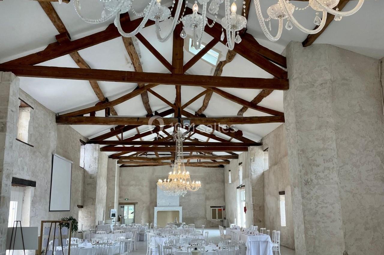 Salle de réception lumineuse avec poutres apparentes, lustres en cristal, fontaine centrale et tables dressées.