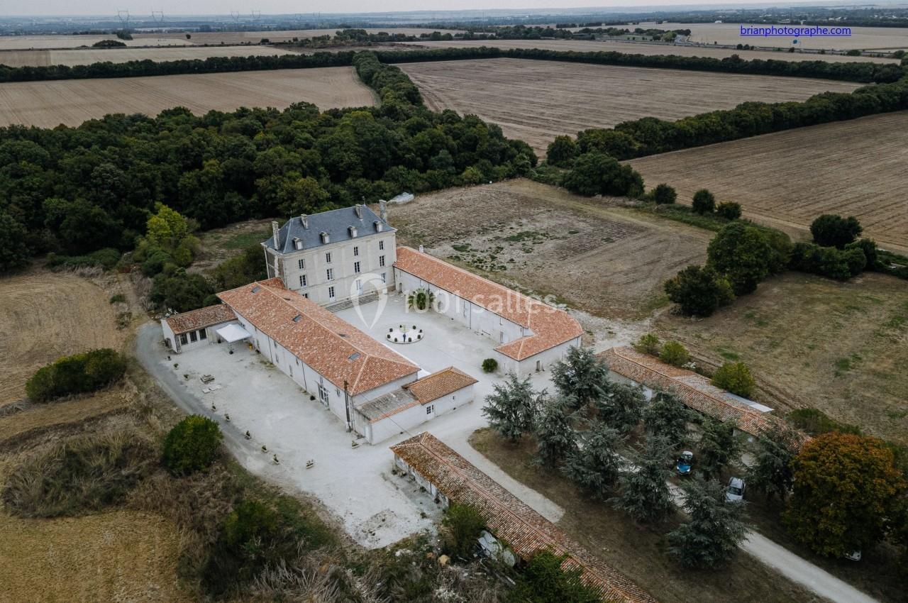 Vue aérienne d'un domaine avec une grande maison principale, des bâtiments annexes et des champs environnants.
