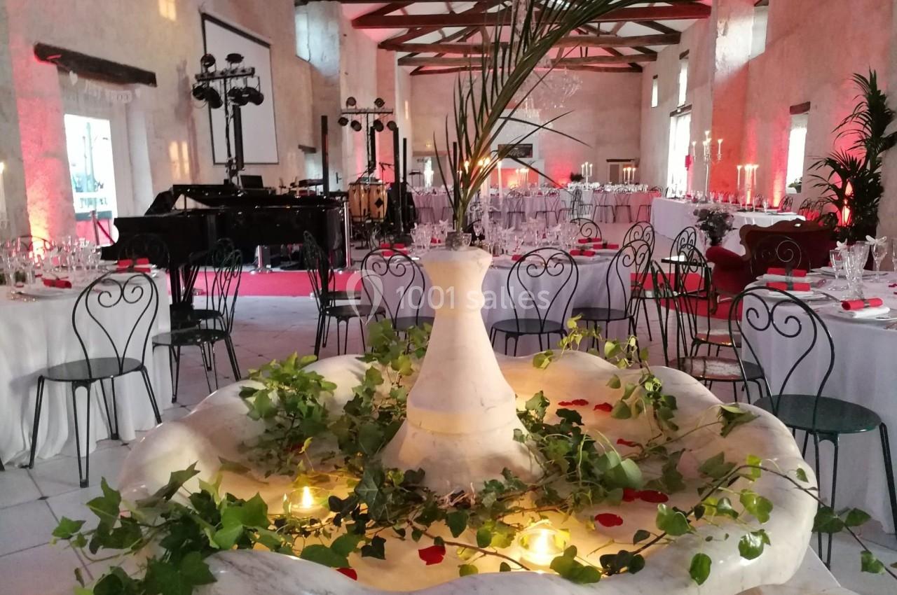 Salle de réception décorée avec des tables dressées, une fontaine ornée de feuillage et de bougies au premier plan.