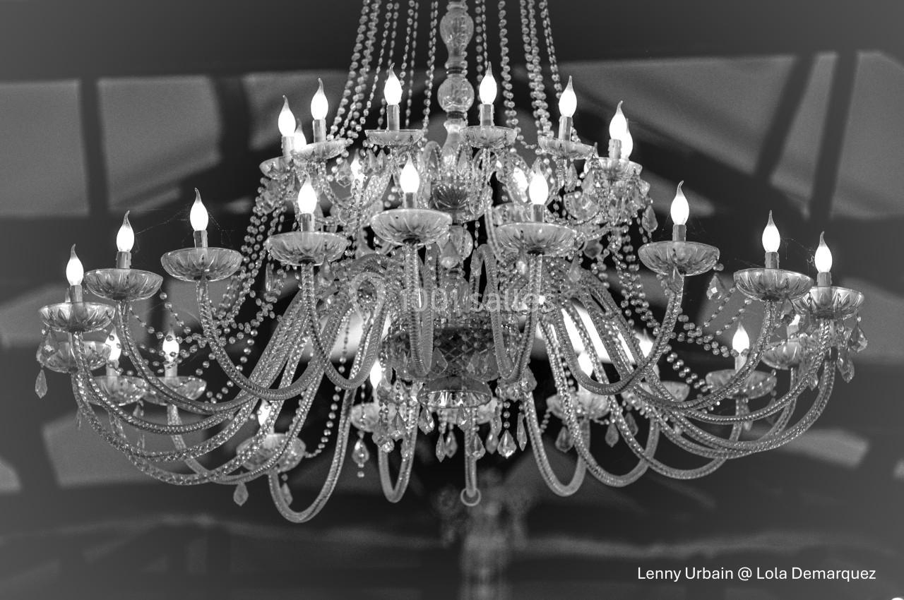 Lustre en cristal allumé, orné de perles et de pampilles, suspendu dans un intérieur sombre avec des poutres visibles.