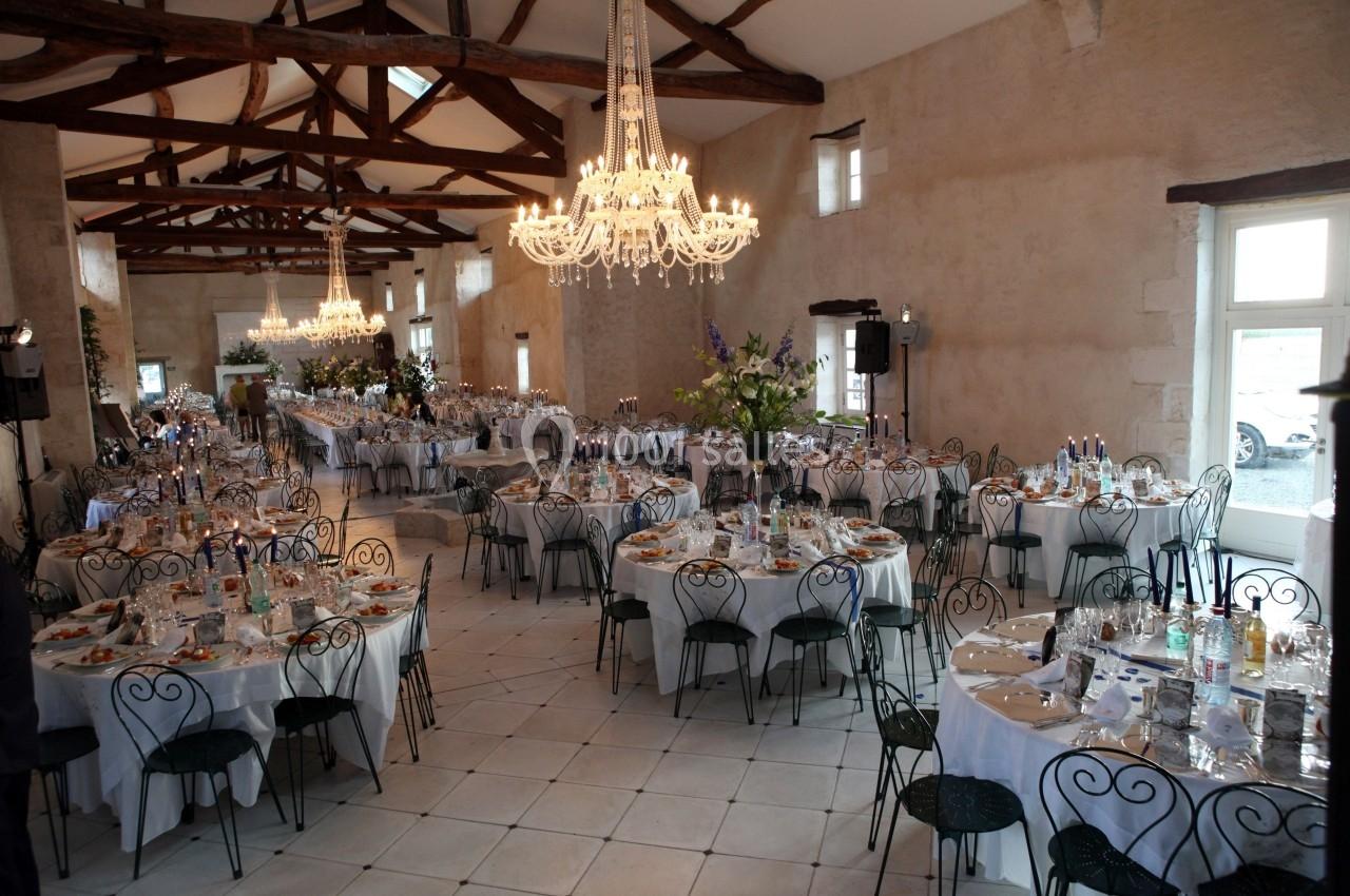 Salle de réception élégante avec tables rondes dressées, chaises en fer forgé et lustres en cristal suspendus.