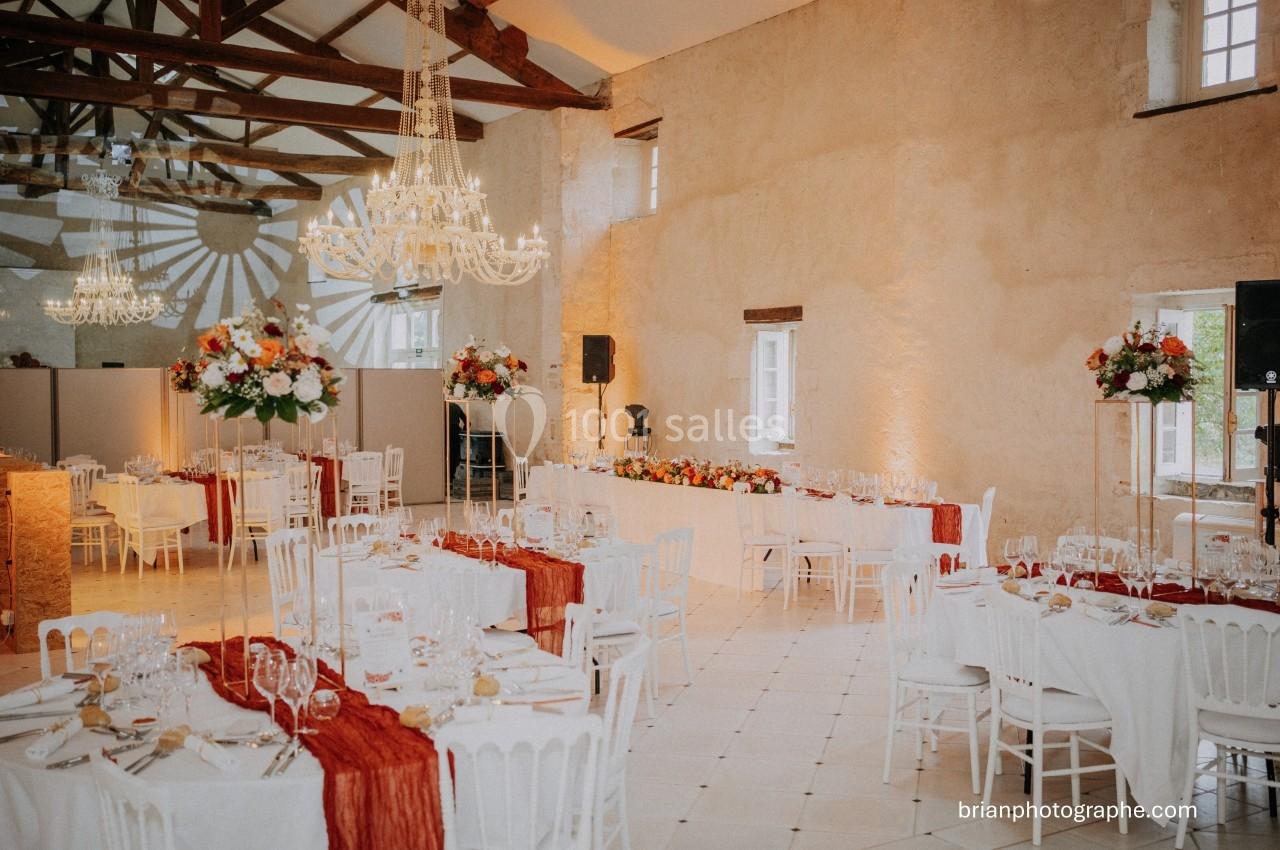 Salle de réception décorée avec des tables dressées, nappes rouges, chandeliers et compositions florales.