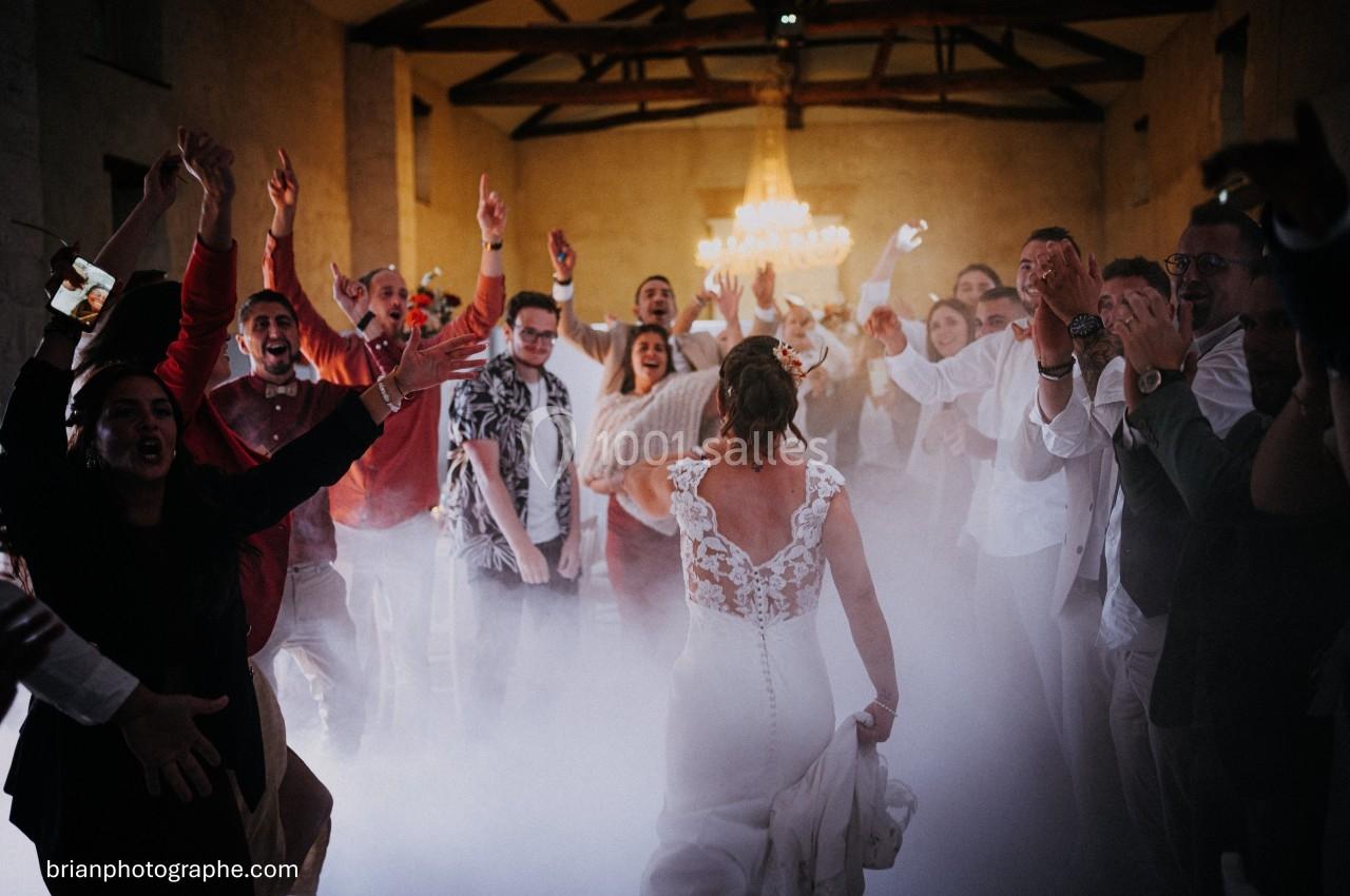 Une mariée en robe blanche danse au centre d'une salle entourée d'invités enthousiastes sous un éclairage chaleureux.