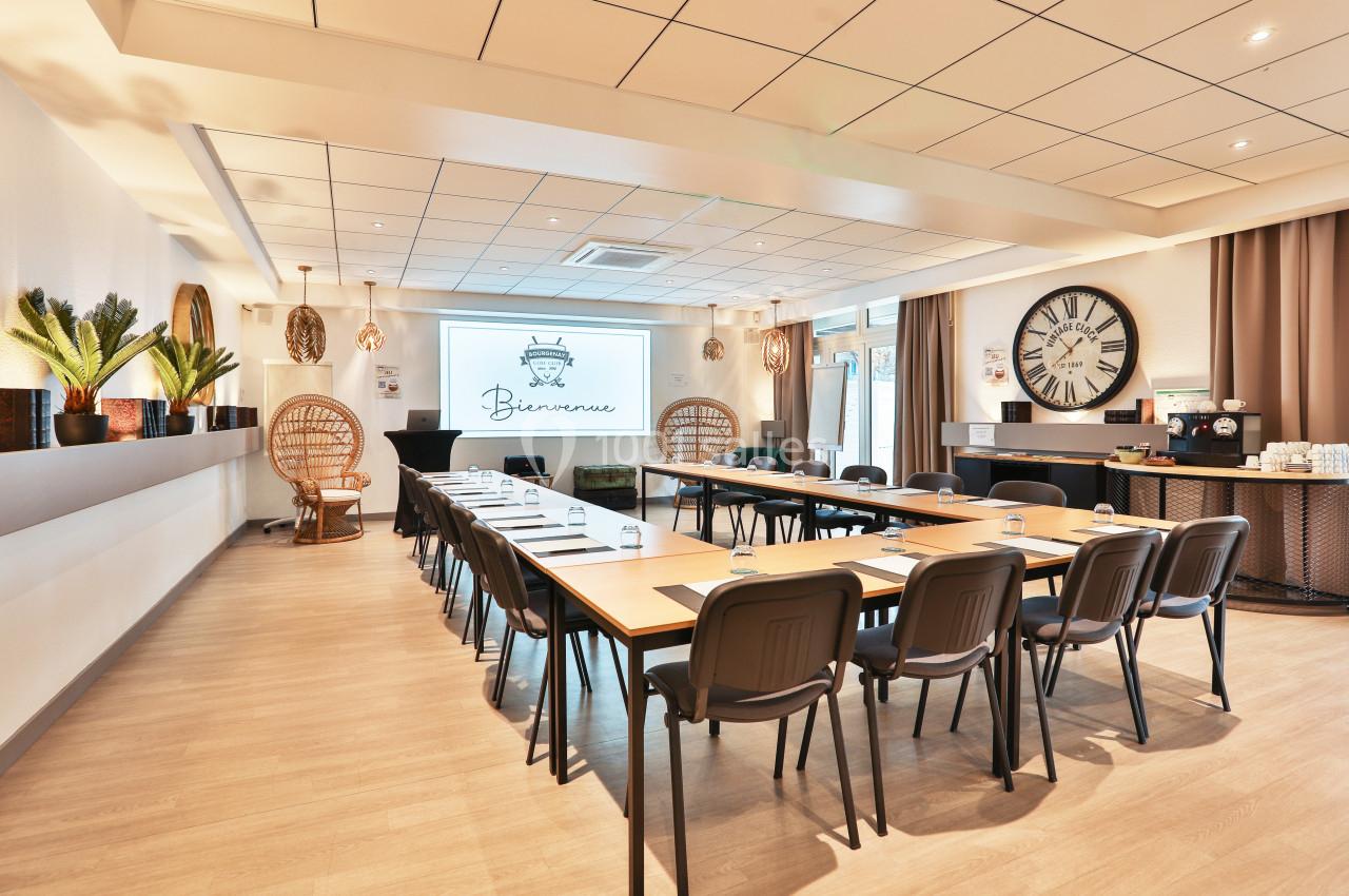 Salle de réunion lumineuse avec tables disposées en U, écran de projection, décorations et coin café.