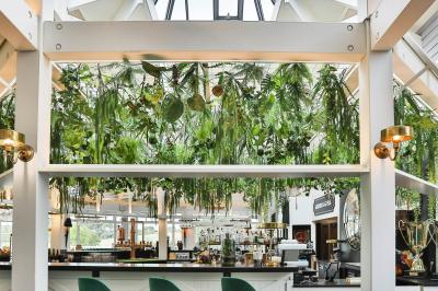 Salle de restaurant lumineuse avec mobilier élégant, banquettes vertes, tables en bois et bar moderne.
