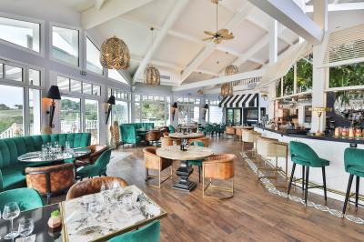 Salle de restaurant lumineuse avec mobilier élégant, banquettes vertes, tables en bois et bar moderne.