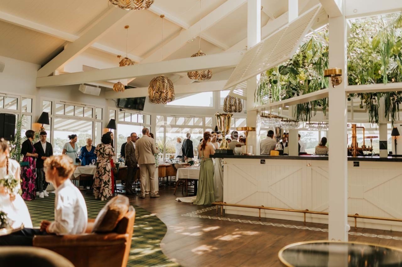 Location salle Talmont-Saint-Hilaire (Vendée) - Bourgenay Golf Club #10 Salle lumineuse avec des invités debout et assis, décorée de plantes suspendues et d'un bar central.