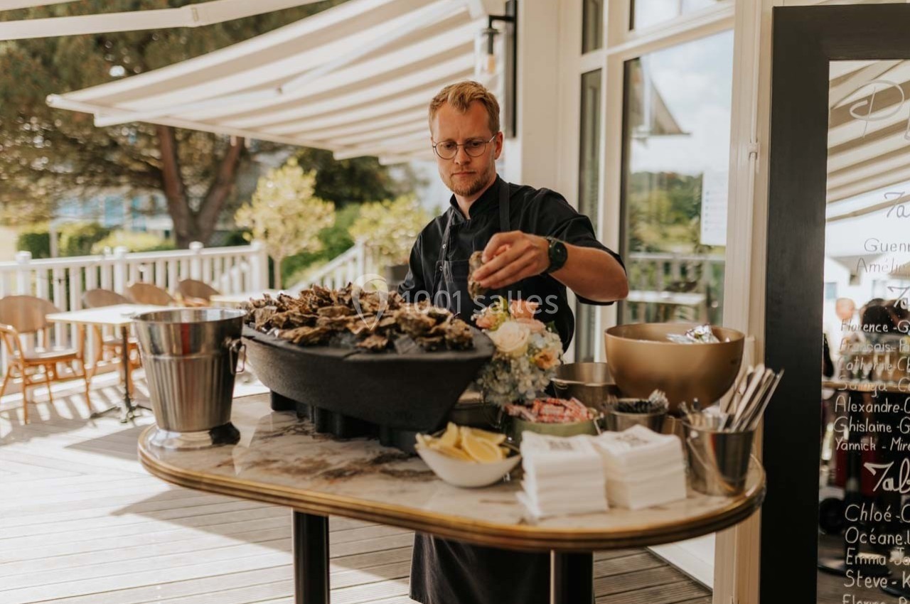 Location salle Talmont-Saint-Hilaire (Vendée) - Bourgenay Golf Club #14 Un homme prépare un plateau d'huîtres sur une terrasse ensoleillée, avec des citrons et des serviettes à disposition.
