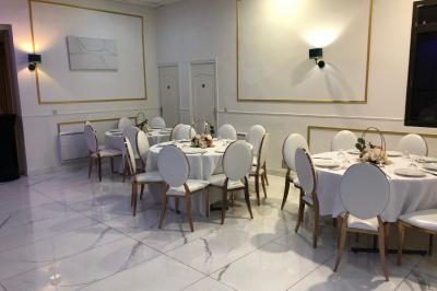 Salle décorée avec des tables rondes dressées, nappes blanches, chaises élégantes et centre de table floral.