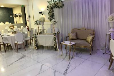 Salle décorée avec des tables rondes dressées, nappes blanches, chaises élégantes et centre de table floral.