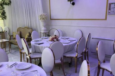 Salle décorée avec des tables rondes dressées, nappes blanches, chaises élégantes et centre de table floral.