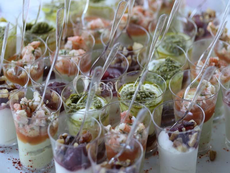 Verrines variées contenant des ingrédients colorés comme crevettes, pesto, fromage et noix, présentées avec des cuillères.