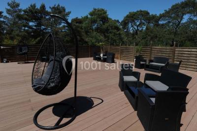 Allée gravillonnée bordée de verdure et de plantes, menant à une entrée avec des arches blanches sous un ciel dégagé.