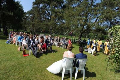 Allée gravillonnée bordée de verdure et de plantes, menant à une entrée avec des arches blanches sous un ciel dégagé.