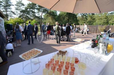 Allée gravillonnée bordée de verdure et de plantes, menant à une entrée avec des arches blanches sous un ciel dégagé.