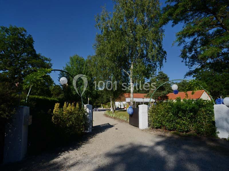 Entrée d'une propriété avec allée gravillonnée, arches décorées de ballons et maison au toit rouge en arrière-plan.