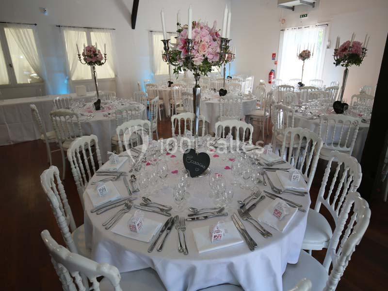 Salle de réception décorée avec des tables rondes, nappes blanches, chaises assorties et centres de table fleuris.