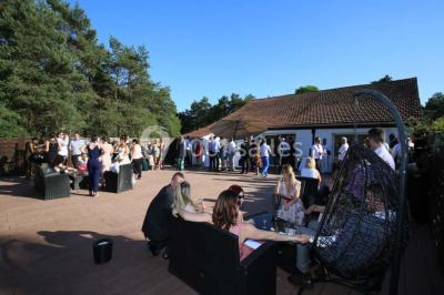Allée gravillonnée bordée de verdure et de plantes, menant à une entrée avec des arches blanches sous un ciel dégagé.