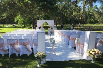 Allée gravillonnée bordée de verdure et de plantes, menant à une entrée avec des arches blanches sous un ciel dégagé.