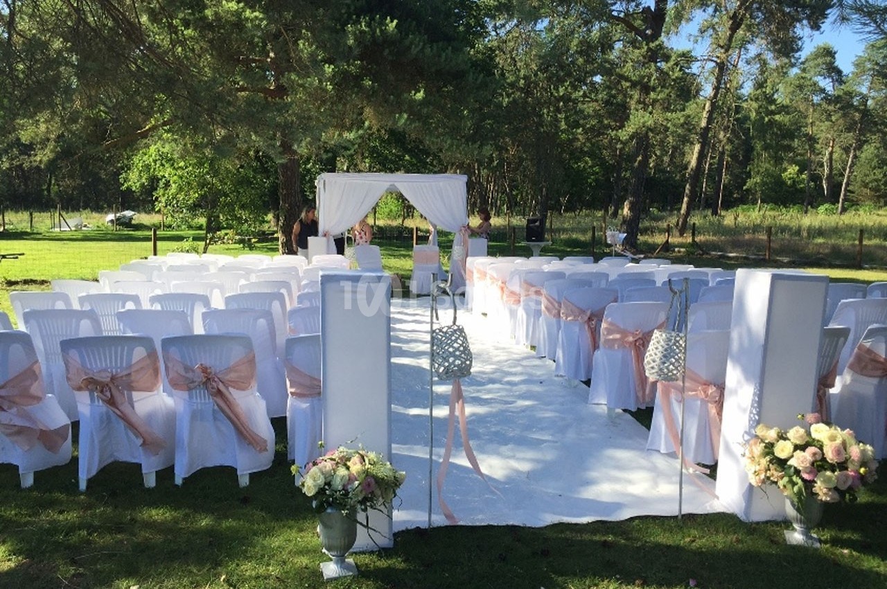 Chaises blanches alignées avec rubans roses et arche décorée, disposées en extérieur pour une cérémonie.