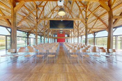 Salle lumineuse avec charpente en bois, tables rondes et chaises, équipée d'un écran de projection.