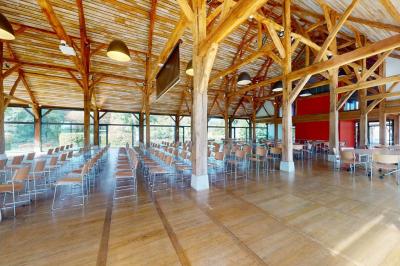 Salle lumineuse avec charpente en bois, tables rondes et chaises, équipée d'un écran de projection.