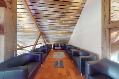 Salle lumineuse avec charpente en bois, tables rondes et chaises, équipée d'un écran de projection.