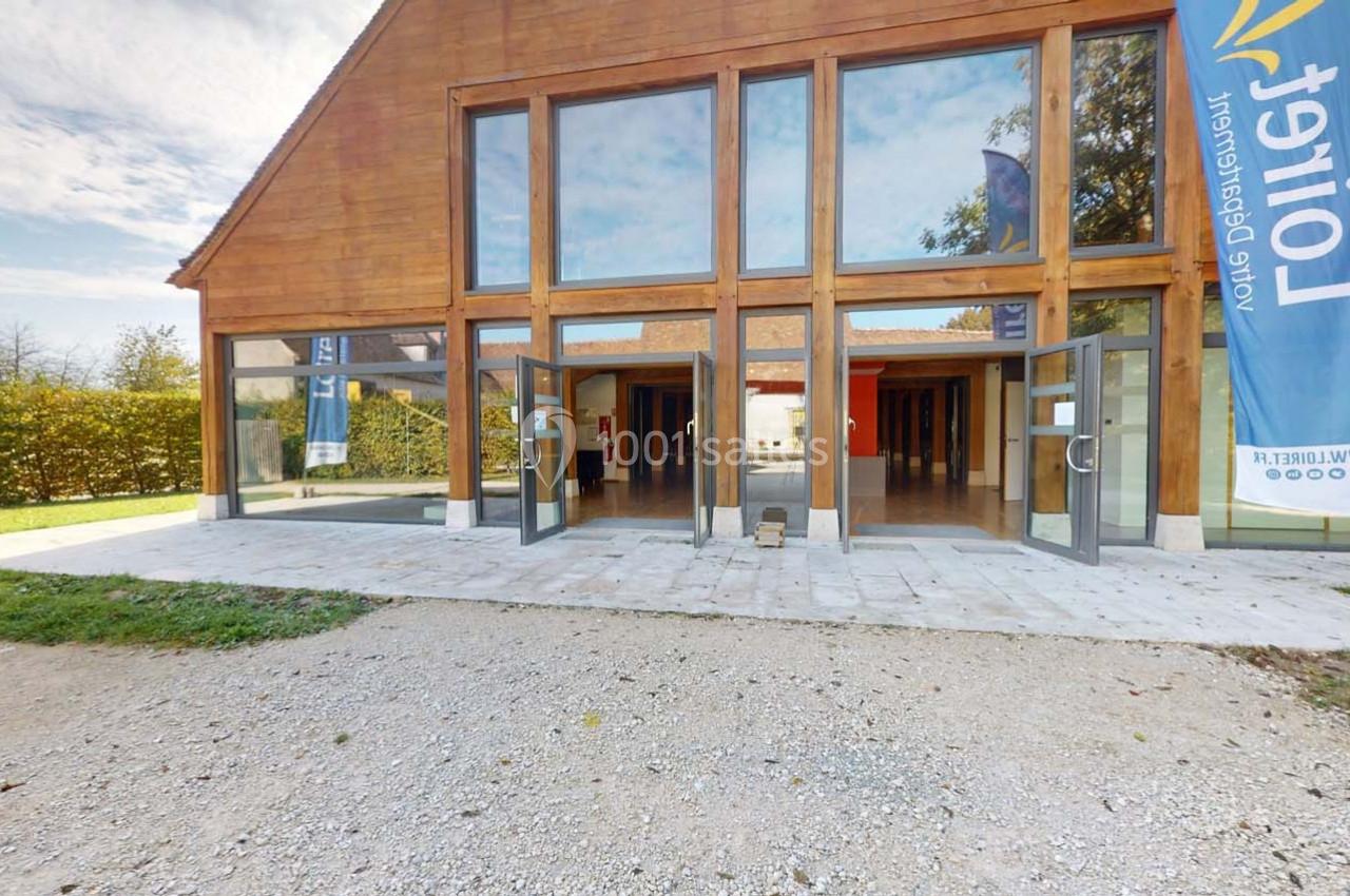 Façade d'un bâtiment en bois avec de grandes baies vitrées et des portes ouvertes, entouré de végétation.