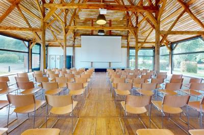 Salle lumineuse avec charpente en bois, tables rondes et chaises, équipée d'un écran de projection.