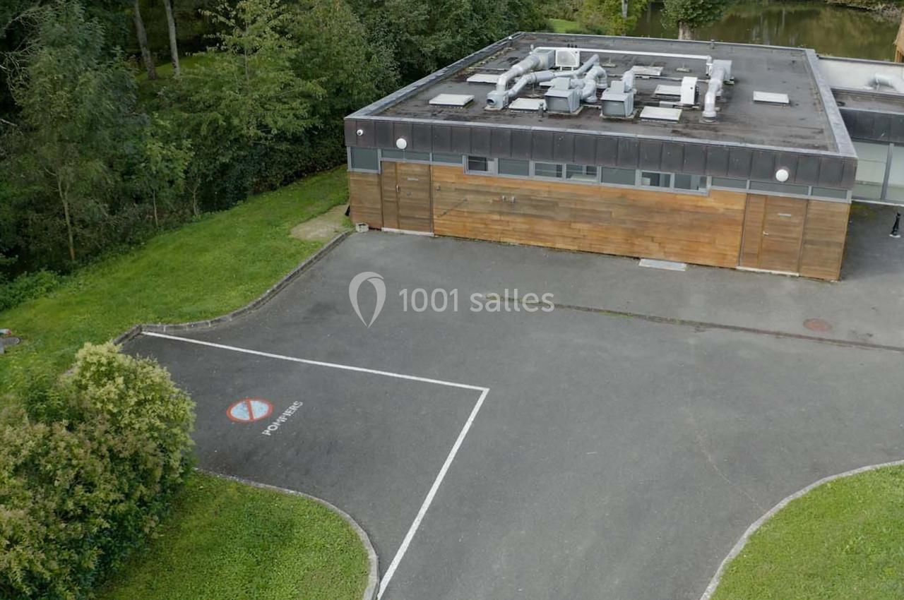Vue aérienne d'un bâtiment rectangulaire en bois entouré de végétation, avec un parking et un panneau ’Interdit’.