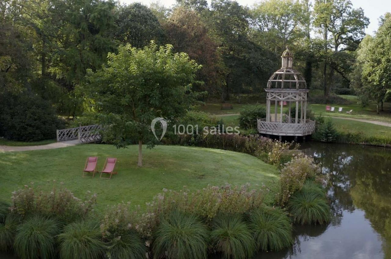 Un jardin verdoyant avec un kiosque en bois près d'un étang et deux chaises longues sur une pelouse.