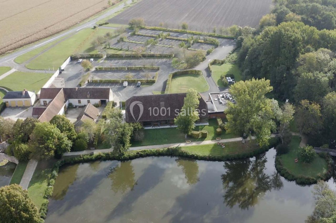 Vue aérienne d'un domaine avec bâtiments, étang, parking et champs environnants, entouré de végétation.