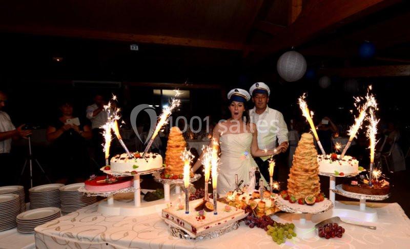 Un couple en tenue de mariage coupe un gâteau entouré de desserts décorés de cierges magiques allumés.